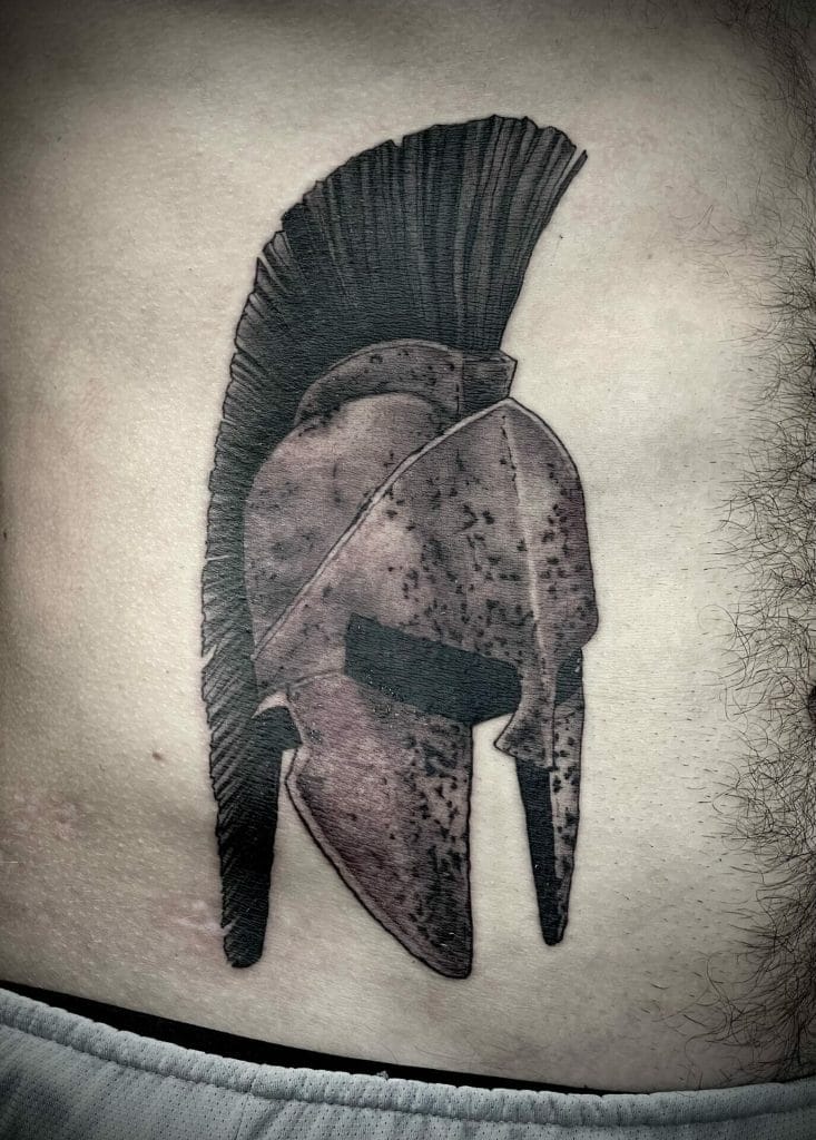 Tattoo of an ancient Greek helmet with a crest on the persons chest.