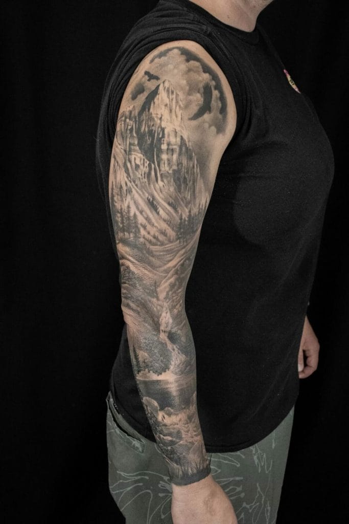 Black and gray mountain landscape tattoo covering the upper arm and forearm.