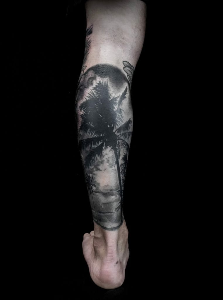 Black and gray tattoo of palm trees and a sunset on a persons forearm.