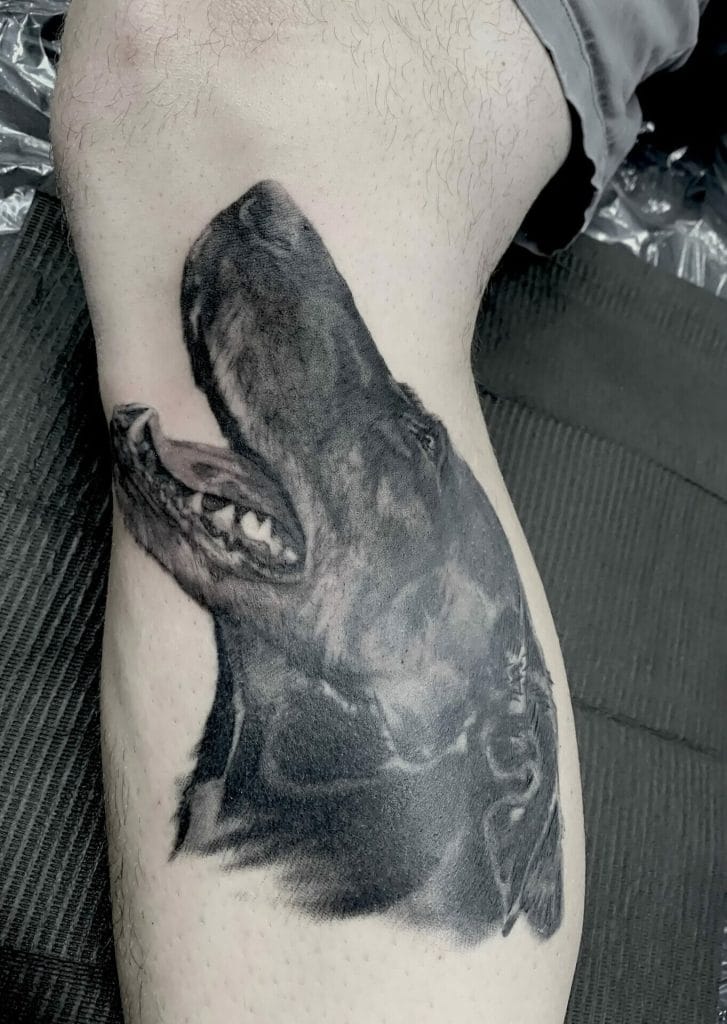 Realistic black and gray tattoo of a dogs head on persons thigh.