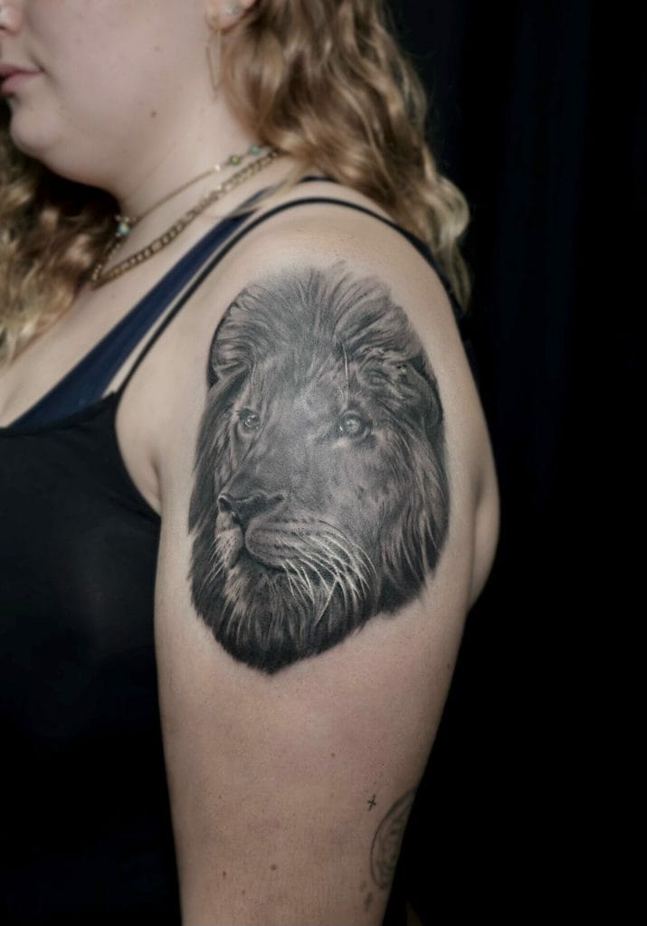 Black and gray lion portrait tattoo on persons upper arm.