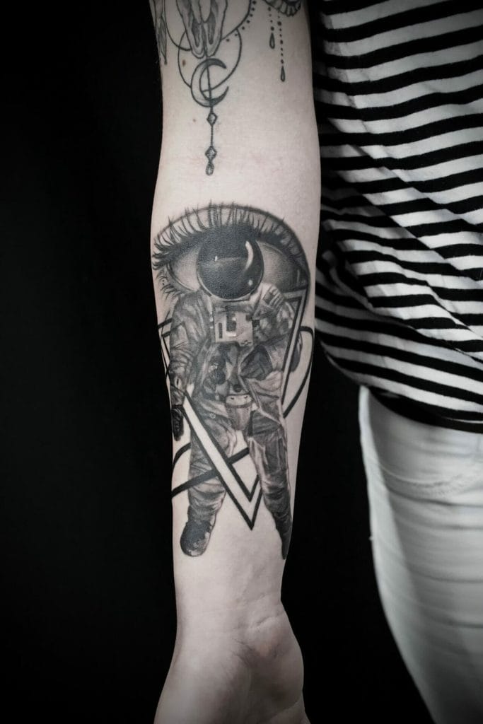 Tattoo of an astronaut with a large eye above, inside a triangle, on a persons forearm.