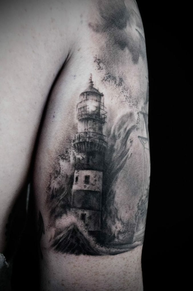 Black and gray lighthouse tattoo on persons upper arm with clouds and waves.