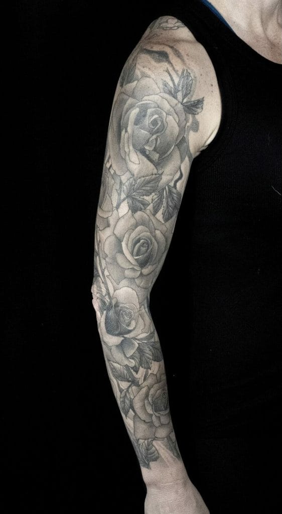 Black and gray floral sleeve tattoo with roses and leaves on persons arm.