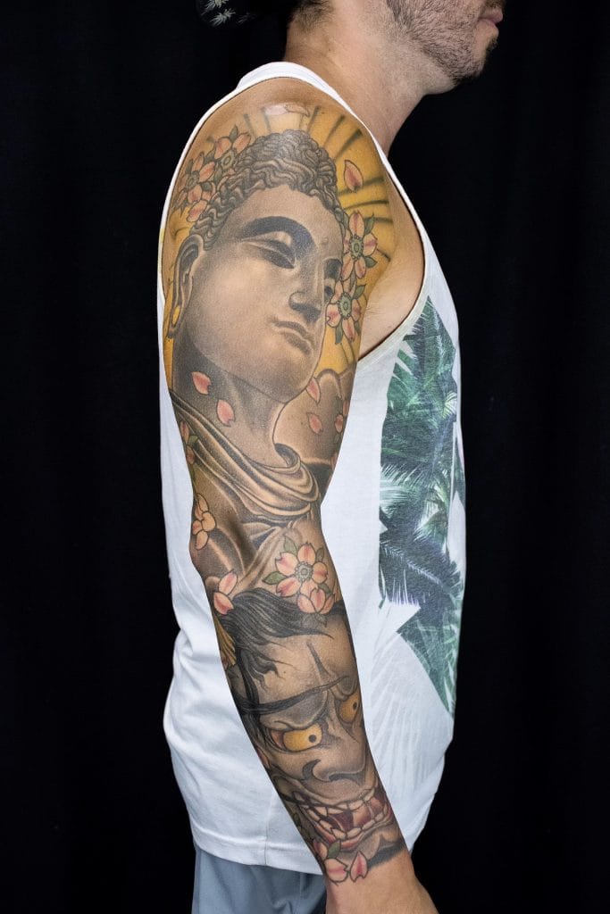 Tattoo of a womans face with flowers and a lion on the arm, visible from the shoulder to the wrist.