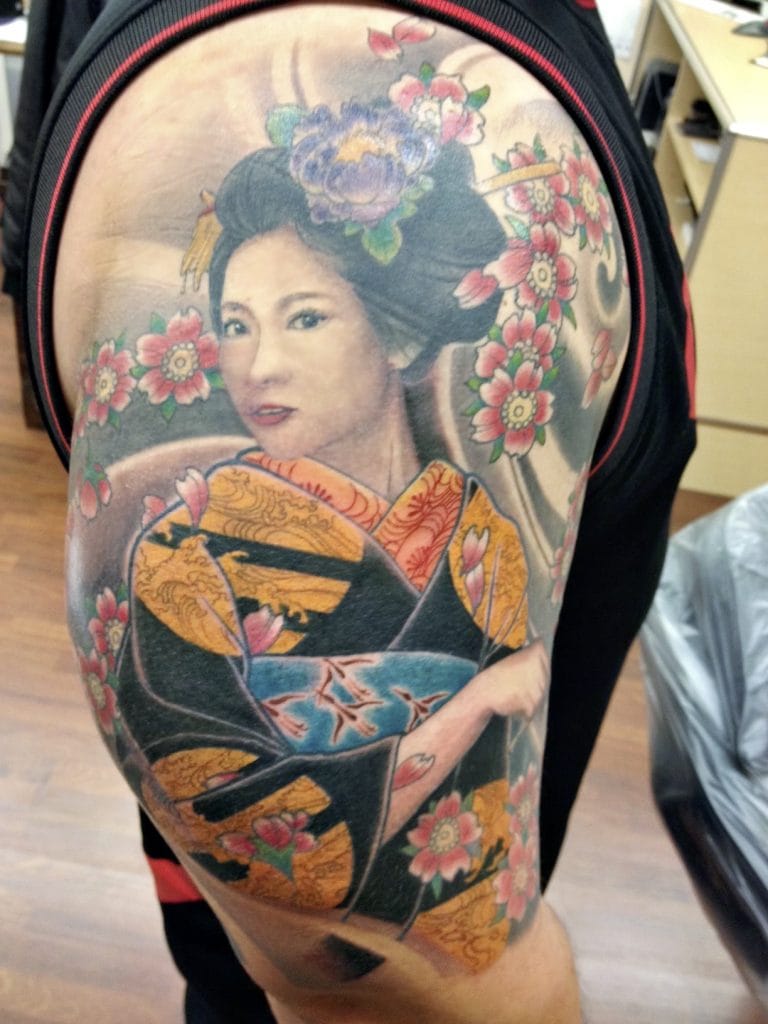 Colorful tattoo of a geisha with flowers on upper arm, wearing a kimono.
