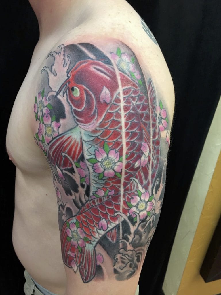 Colorful koi fish tattoo with pink cherry blossoms on persons upper arm and shoulder.