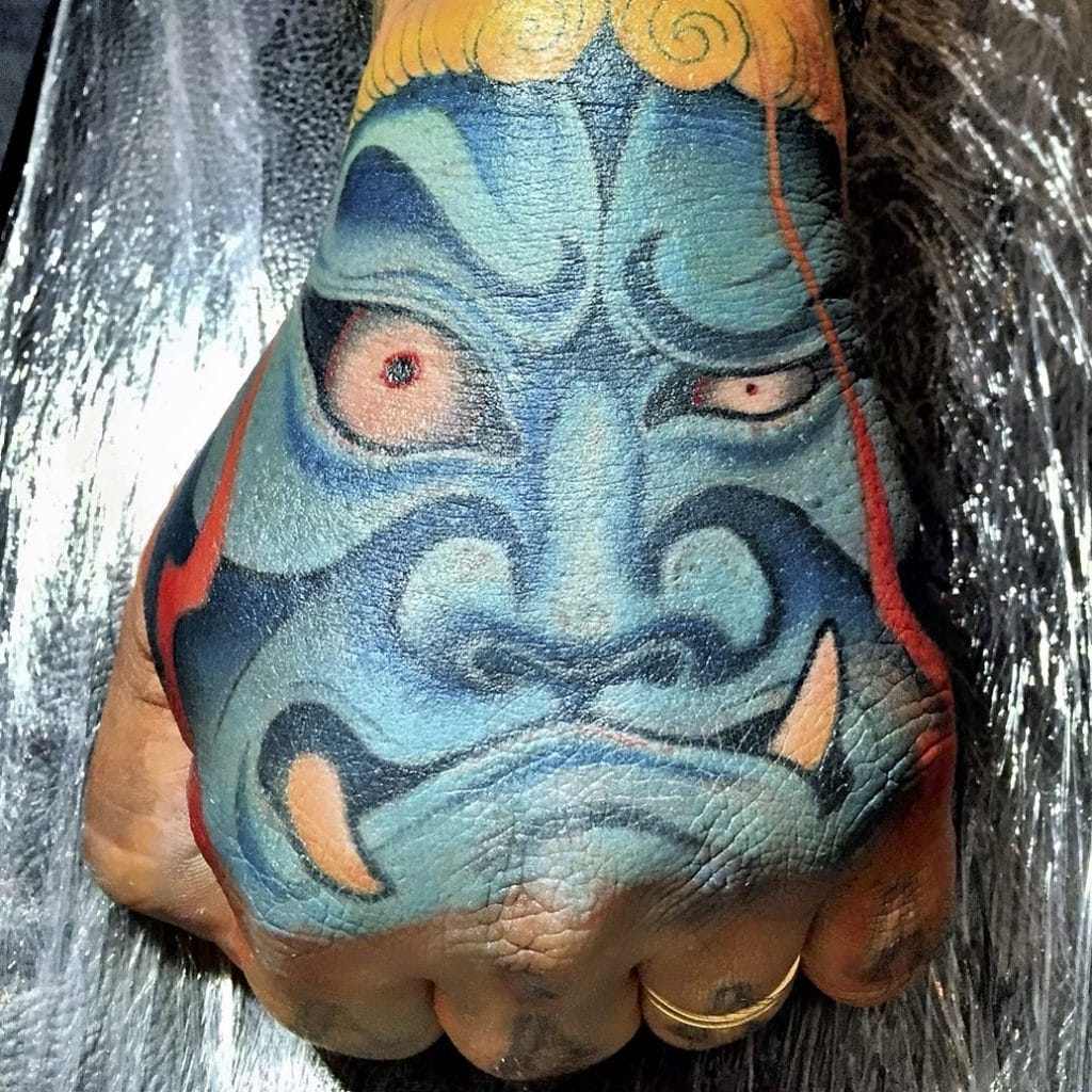 Colorful traditional Japanese Hannya mask tattoo covering the hand and wrist.