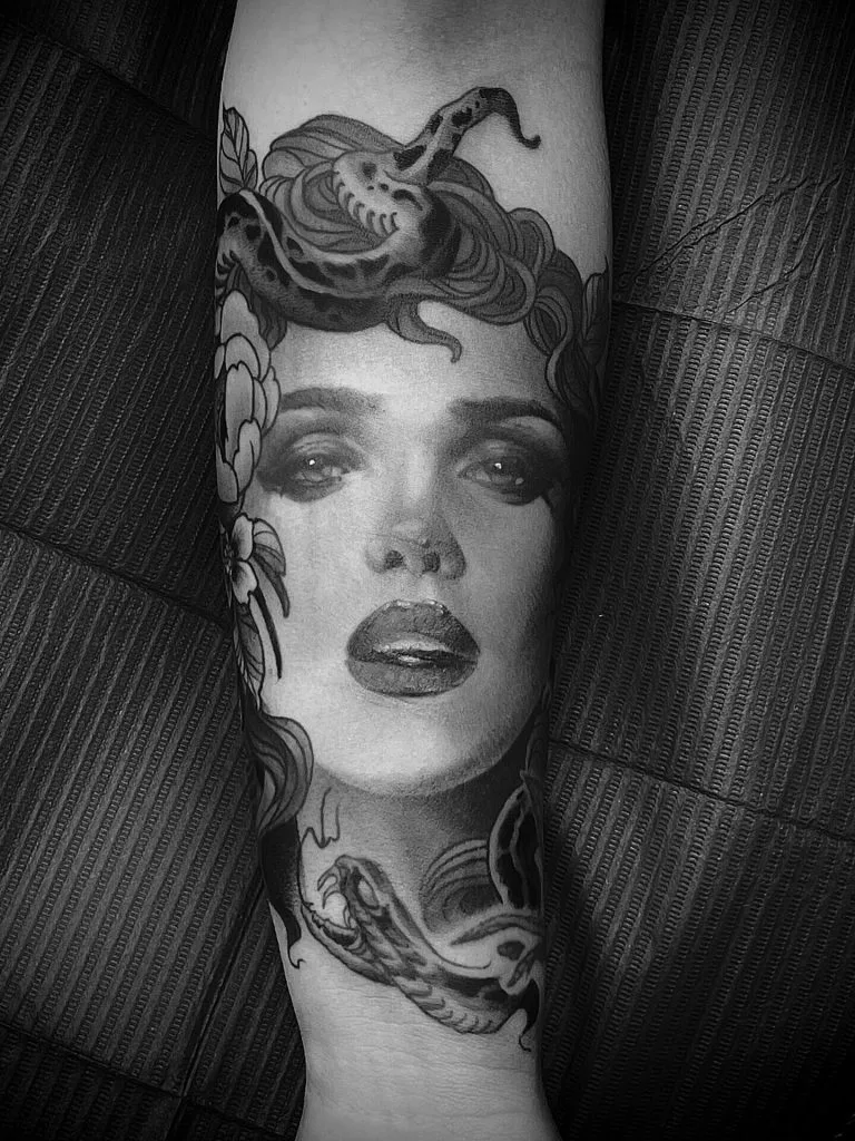 Tattoo of a womans face with flowing hair and a snake on her head.