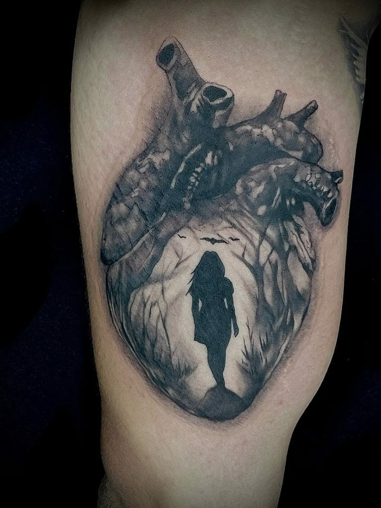 A detailed black and gray tattoo of a human heart with a silhouette of a woman walking through a cave inside it.