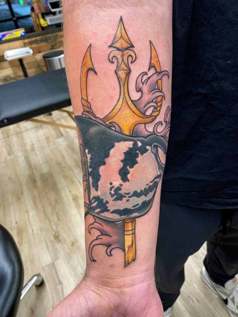 Tattoo of a black and gray mug with a dark liquid, behind a golden trident with purple smoke.