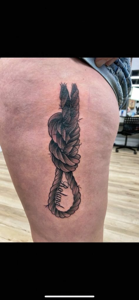 A tattoo of a knotted rope with the word believe inside the loop on a persons thigh.