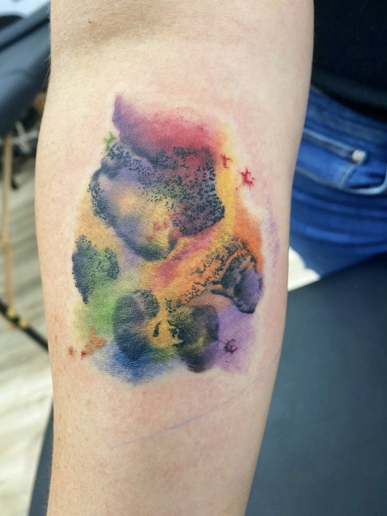 Colorful watercolor-style skull tattoo with black, purple, green, yellow, and orange hues.