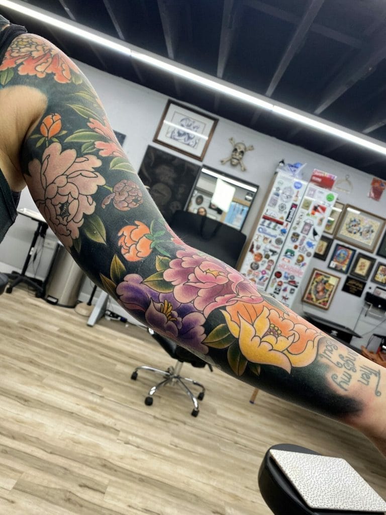 Colorful floral tattoo sleeve with pink, purple, orange, and yellow flowers on arm.