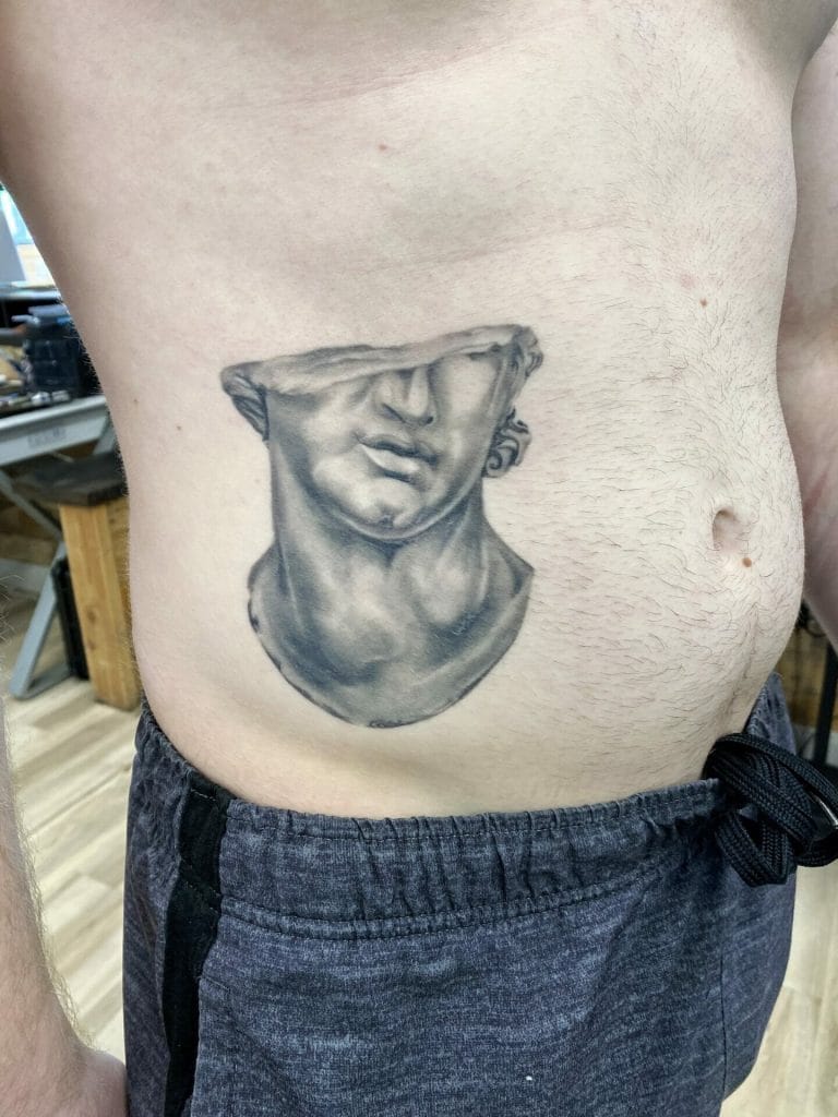 Black and gray tattoo of a classical sculpture bust on persons side torso.