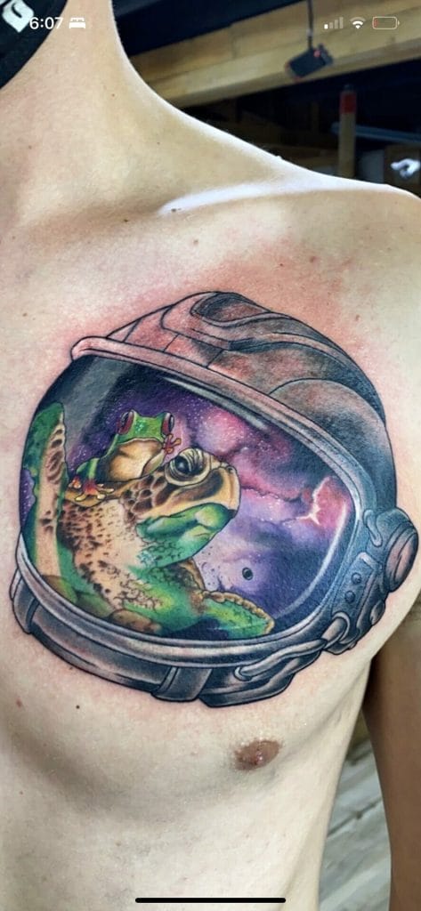 Lizard with a frog on its back inside a space helmet with a galaxy background.