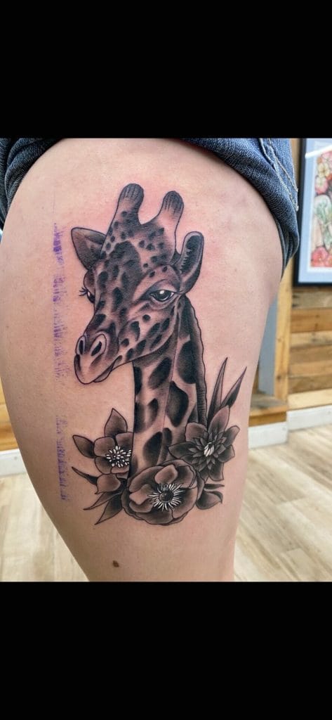 Giraffe with flowers tattooed on persons thigh, black and gray shading.