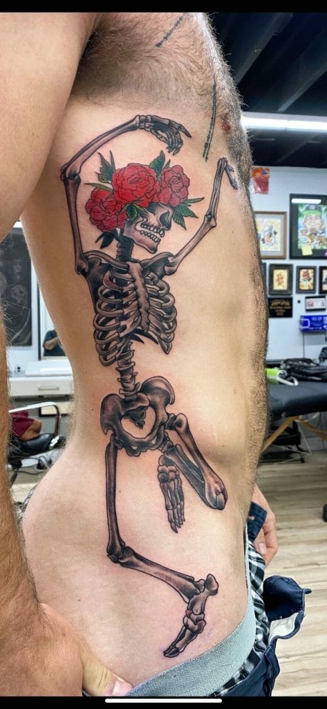 Skeleton with a skull holding a bouquet of red roses over its face on persons side.