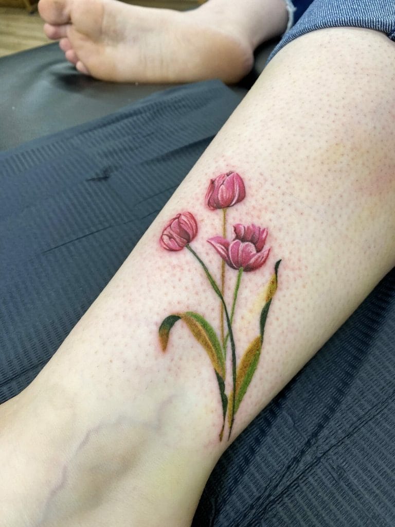 Colorful tulip tattoo on persons lower leg with green leaves and stems.