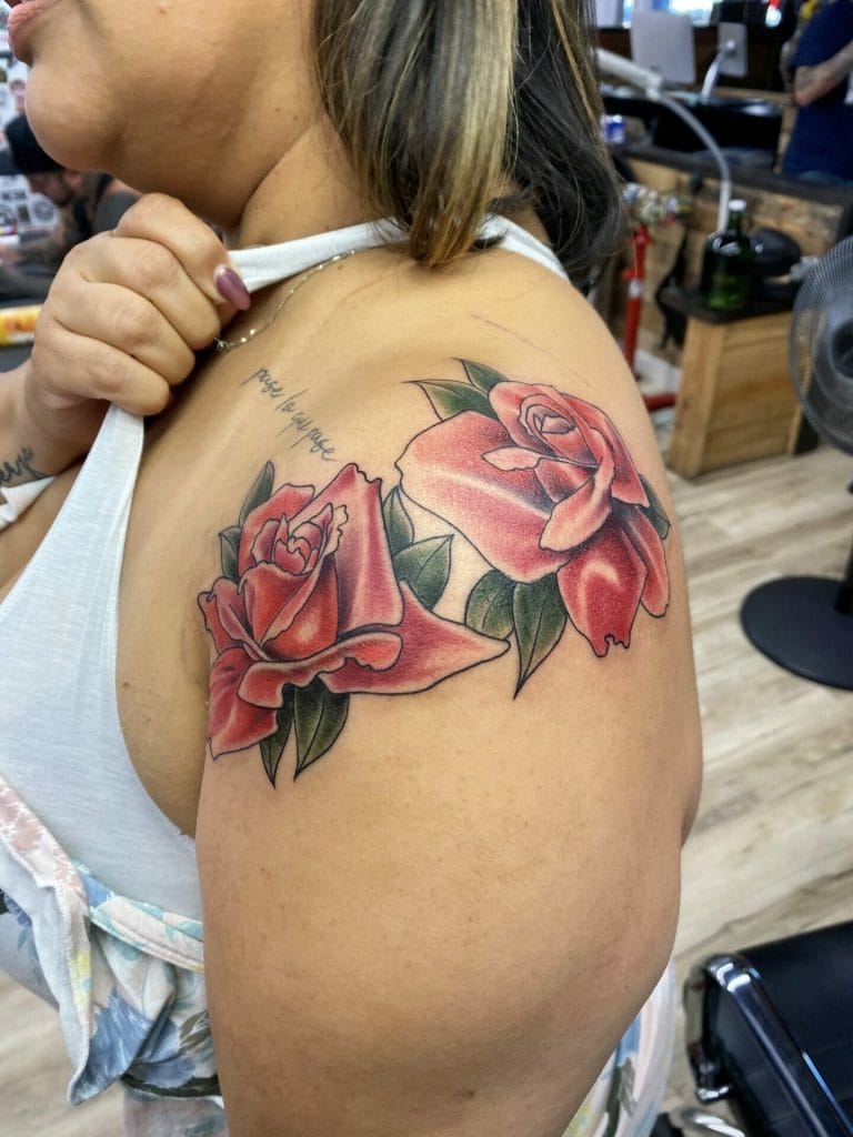 Pink roses with green leaves tattoo on womans shoulder and upper arm.