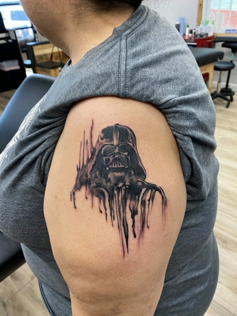 Black and gray tattoo of Darth Vaders helmet with dripping, abstract design on upper arm.