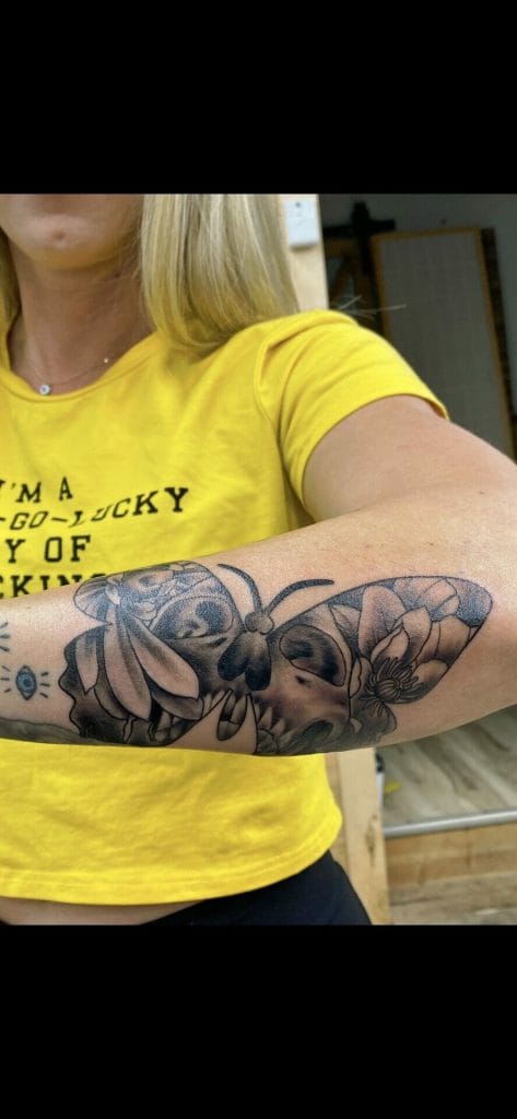 Tattoo of a large bee and flowers on a persons forearm, with part of a yellow shirt visible.