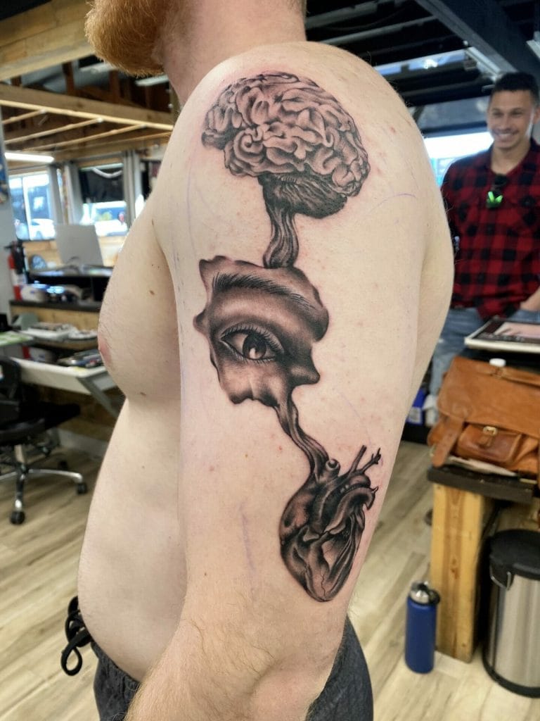 Tattoo of a brain, eye, and heart connected by smoke or steam on mans upper arm.