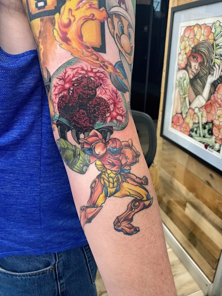 Colorful tattoo of a robotic animal, a mushroom, and a character with a helmet on arm.