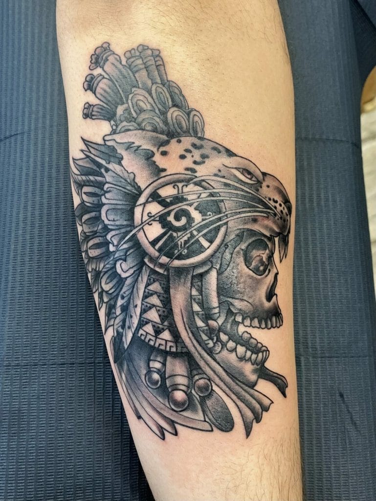 Jaguar head with a skull, feathers, and tribal patterns in black and gray tattoo style.