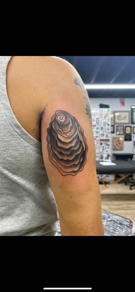 Black and gray layered rose tattoo on upper arm, with tattoo shop background.