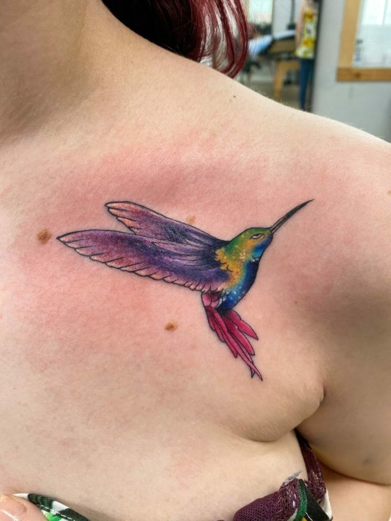 Colorful hummingbird tattoo on persons shoulder with purple, green, blue, and pink hues.