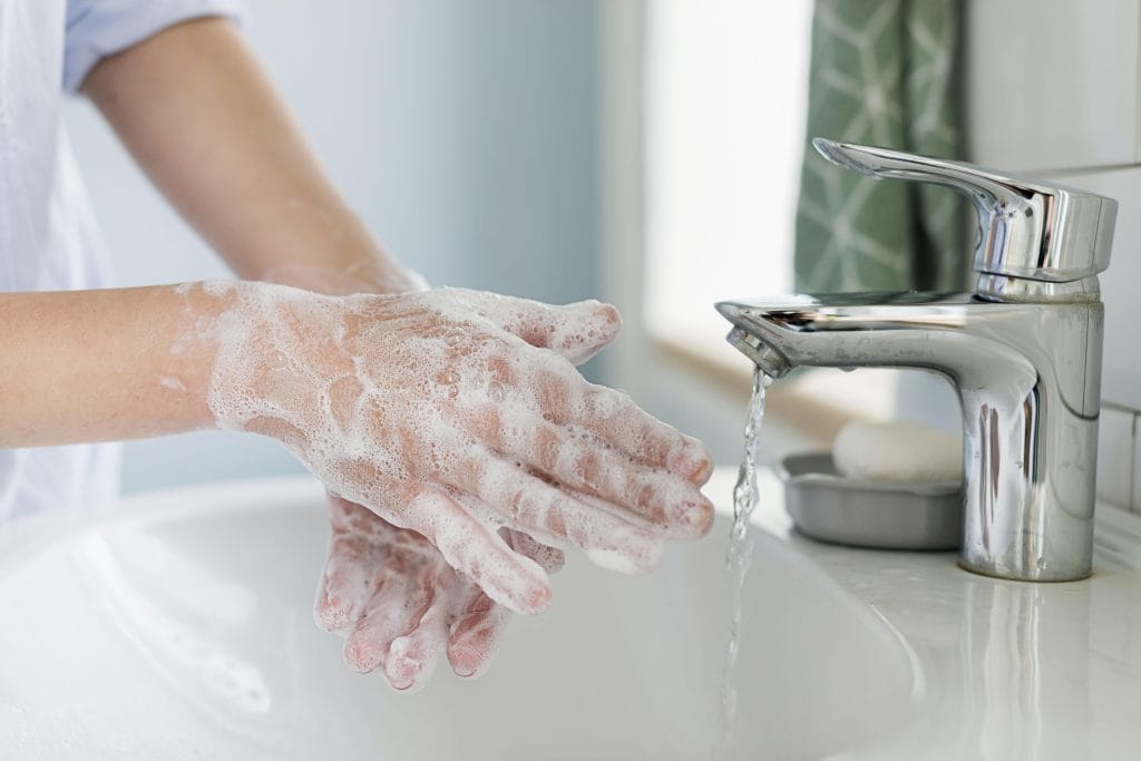 A person washing their hands with soap at a sink, next to running water and a bar of soap on a dish—a crucial step in fresh tattoo care, especially after working out or going to the gym after getting a tattoo.