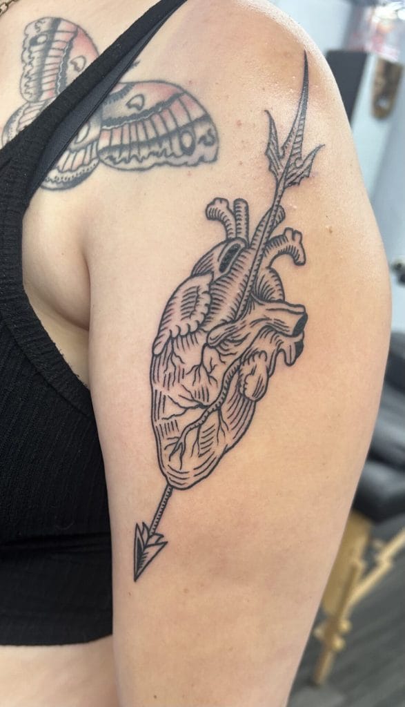 Detailed black line tattoo of a realistic human heart pierced by an arrow on upper arm.
