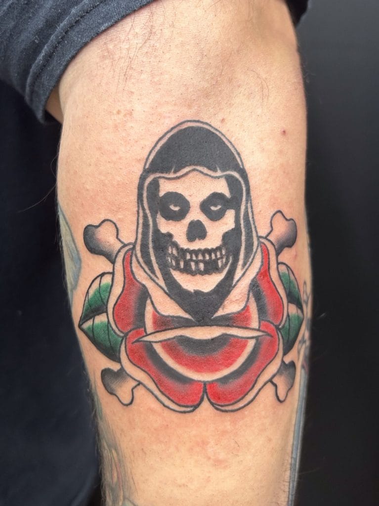 Skull with a hood above a red and green rose, with bones crossed behind.