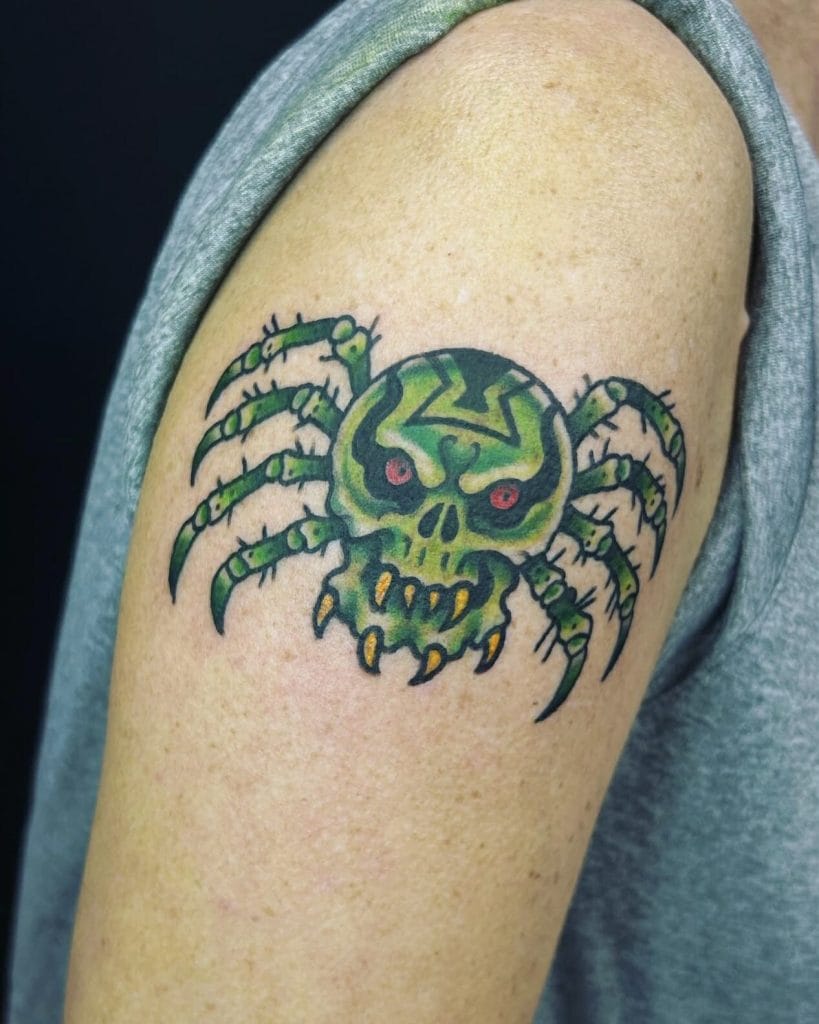 Green spider with a skull face and red eyes tattoo on upper arm.