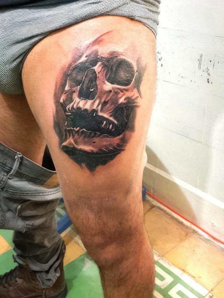 Black and gray skull tattoo on persons upper thigh, with detailed shading and depth.