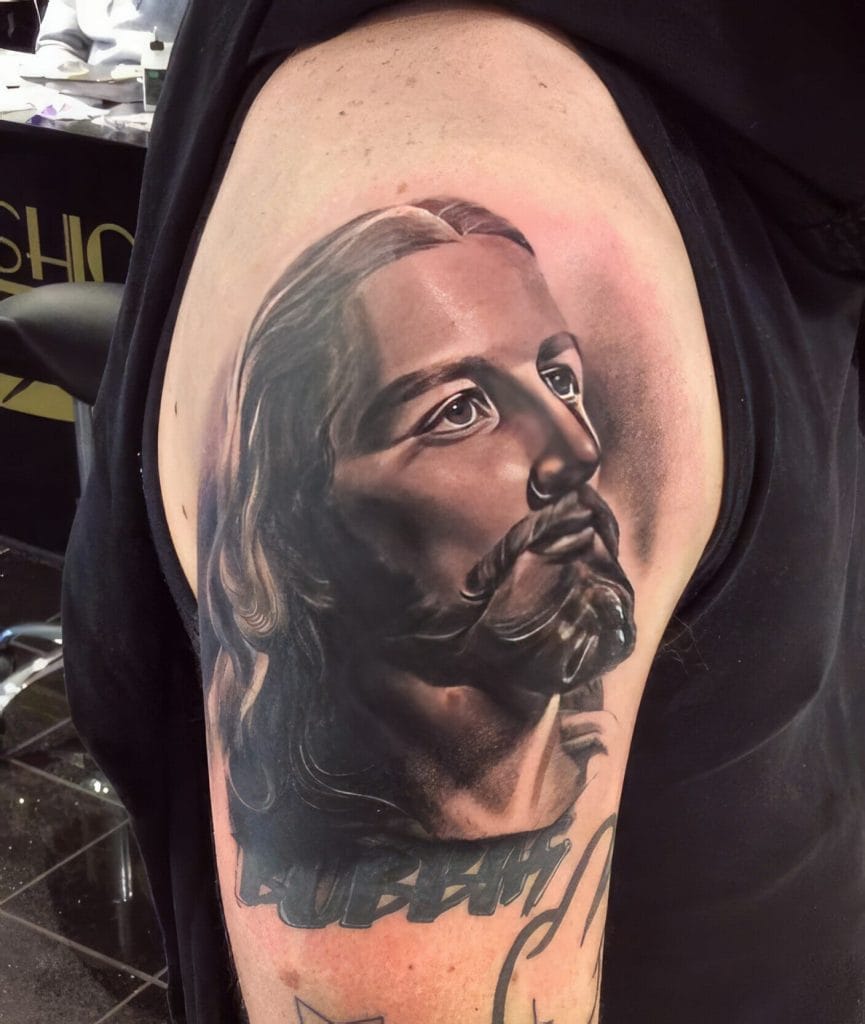 Realistic black and gray tattoo of Jesus Christs face on persons upper arm.