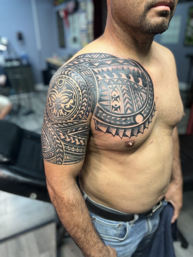 Black Polynesian tribal tattoo covering the shoulder and upper arm of a shirtless man.