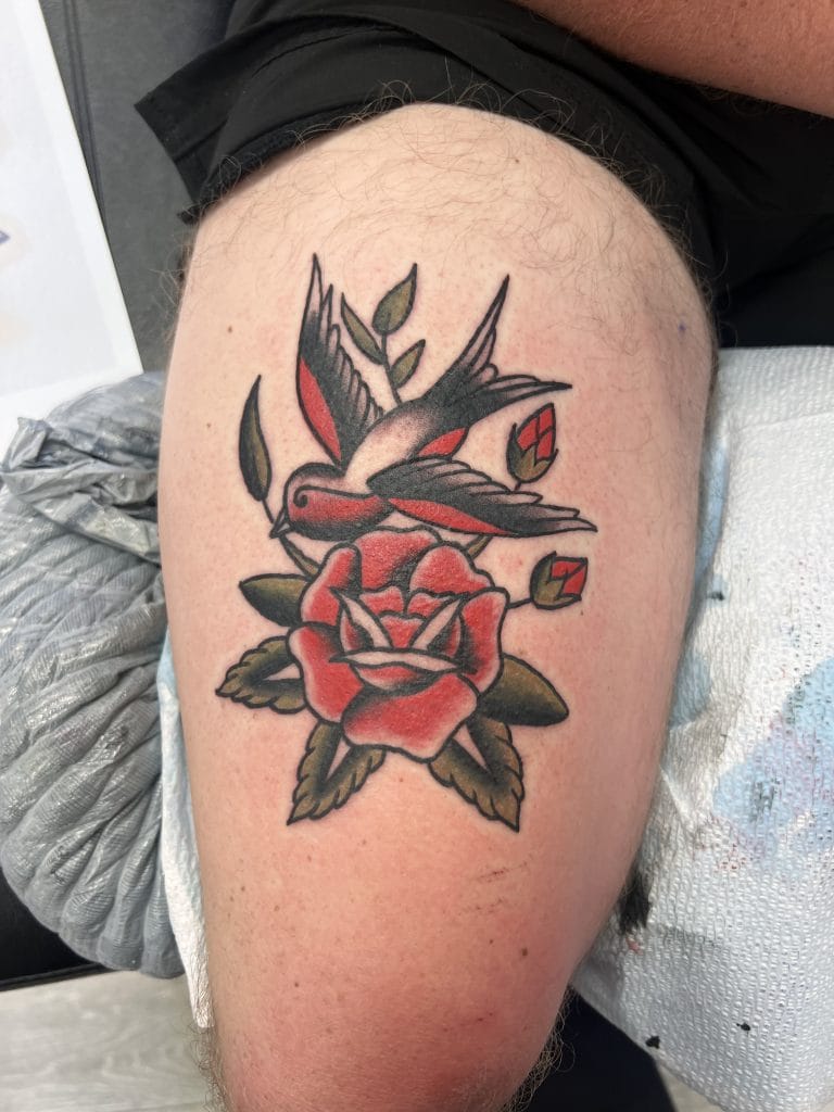 A traditional-style tattoo of a hummingbird hovering above a red rose with green leaves.