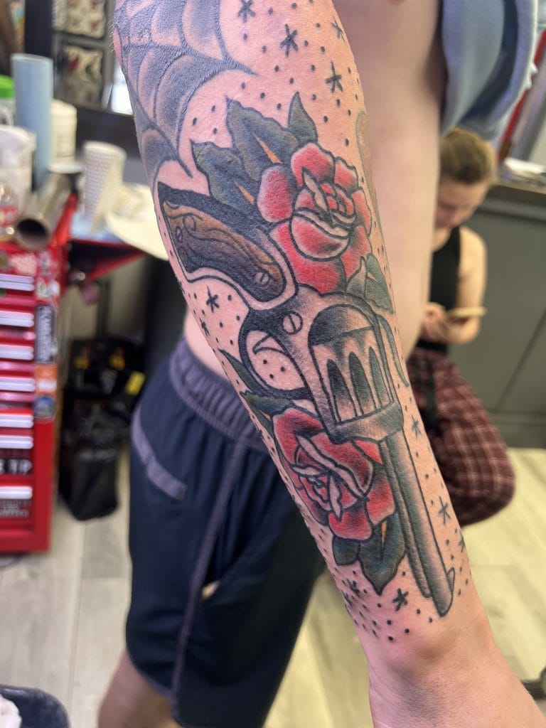 Tattoo of a rose, dagger, and stars on persons forearm with bold outlines and shading.