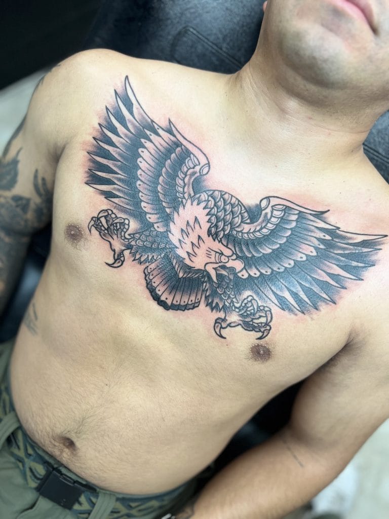 Large black and gray eagle tattoo across the persons chest with wings spread wide.