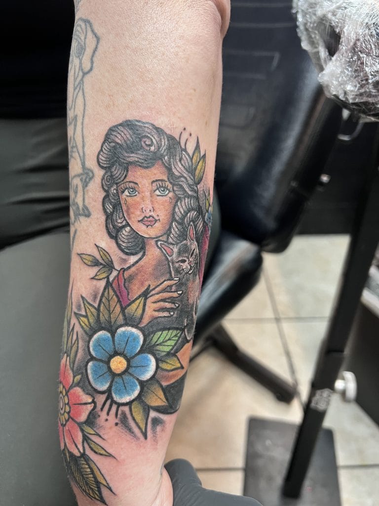 Woman with curly hair holding a cat, surrounded by colorful flowers and green leaves.