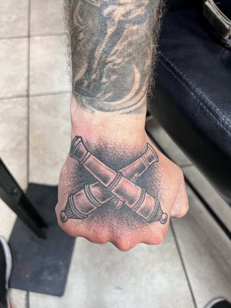 Tattoo of two crossed bullets on the hand with a shaded background.