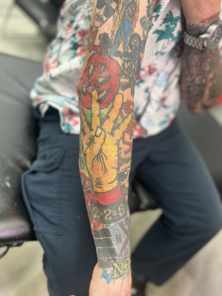 Tattooed arm with a peace sign, red and yellow colors, and the date 2.2.5.