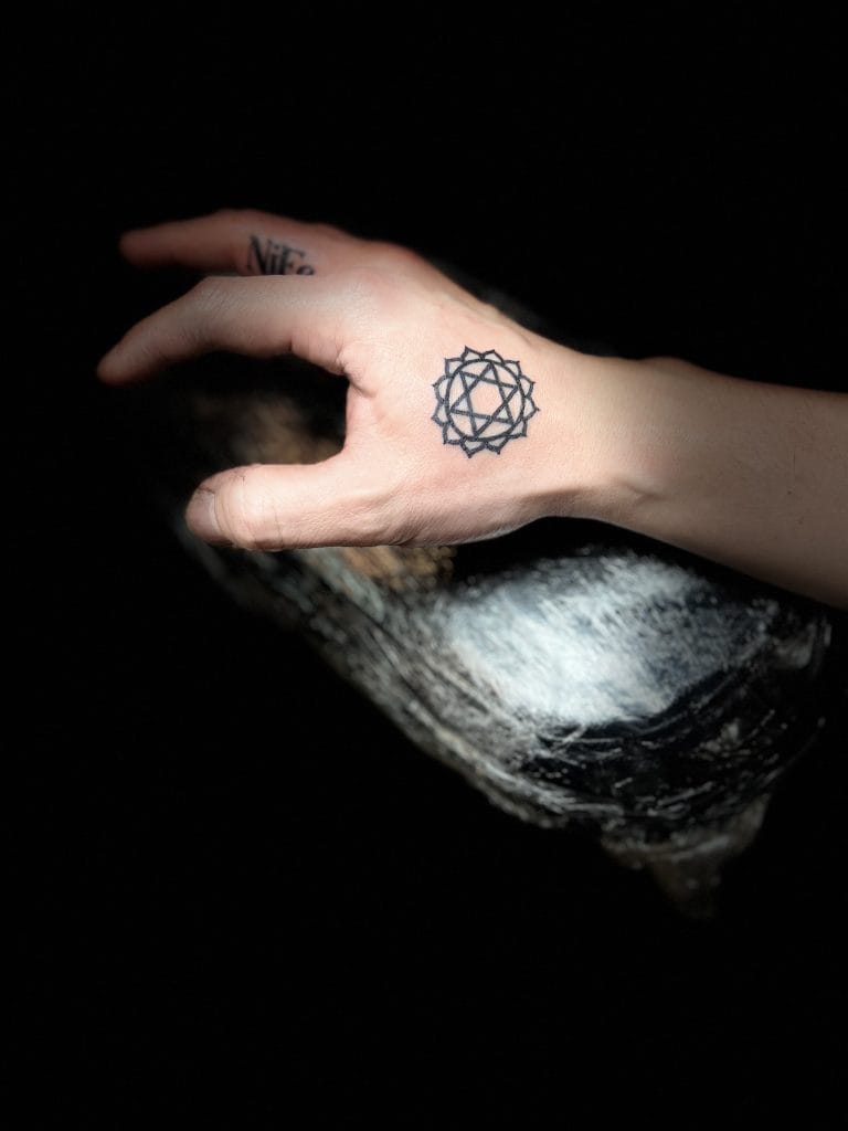 Hand with a geometric tattoo on the back, holding a black and white object against a dark background.