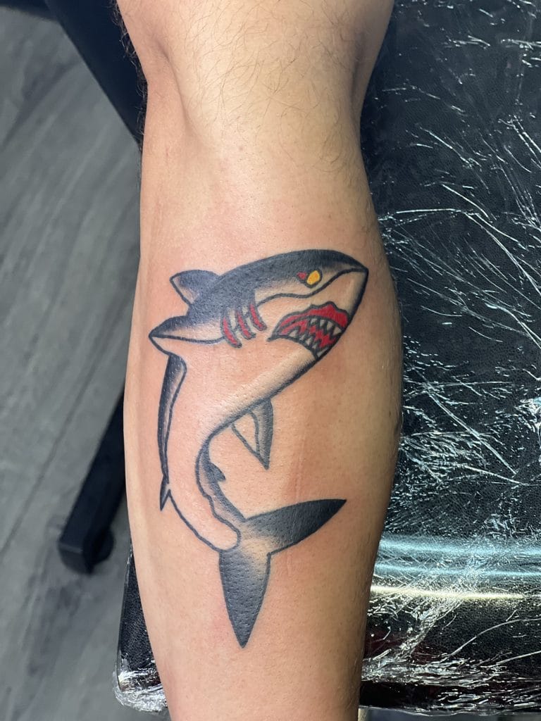 Shark with red teeth, yellow eye, and black outline on persons forearm.