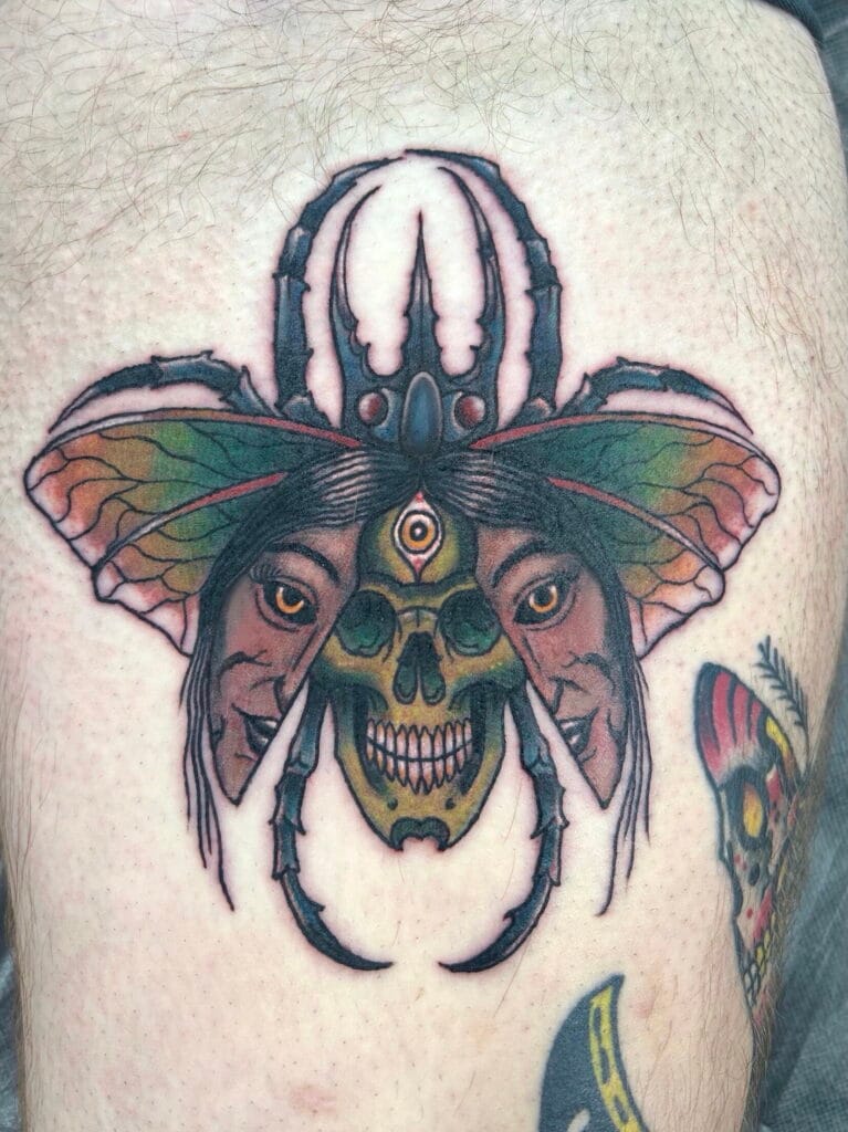 A tattoo featuring a skull with a third eye, butterfly wings, and a spider above it.