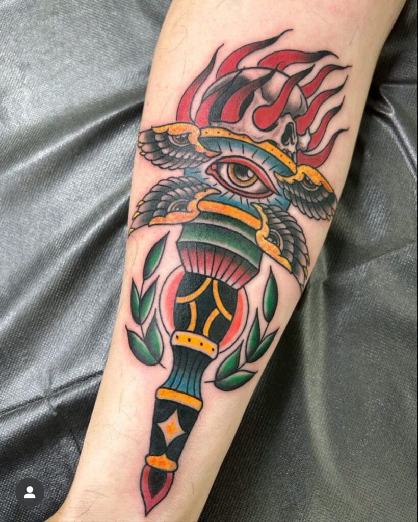 Tattoo of an eye with wings, skull, flames, and a dagger with green leaves.